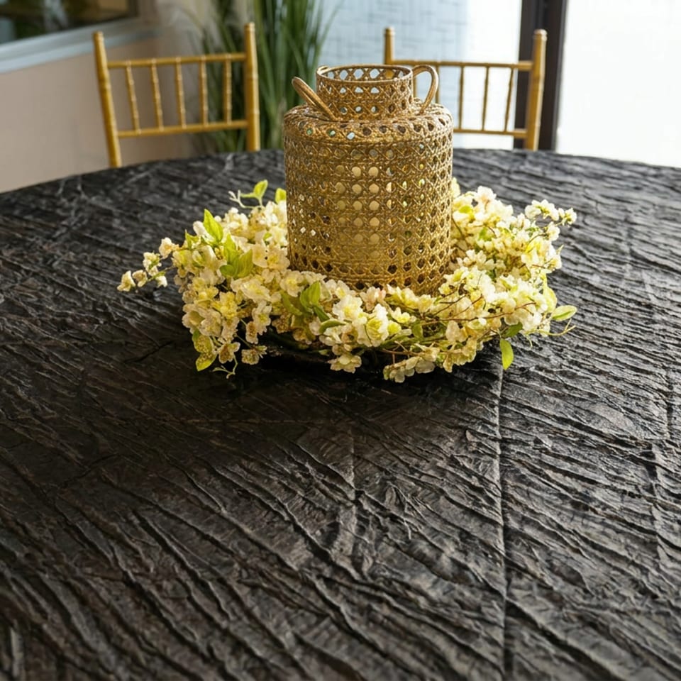 Black textured dining table with a gold lantern centerpiece surrounded by white flowers and gold Chiavari chairs.