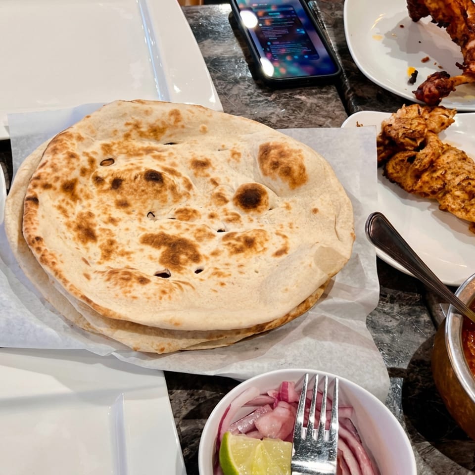 Indian meal spread with stacked naan, grilled kebabs, fried skewers, spiced curry, and pickled onions on white plates.