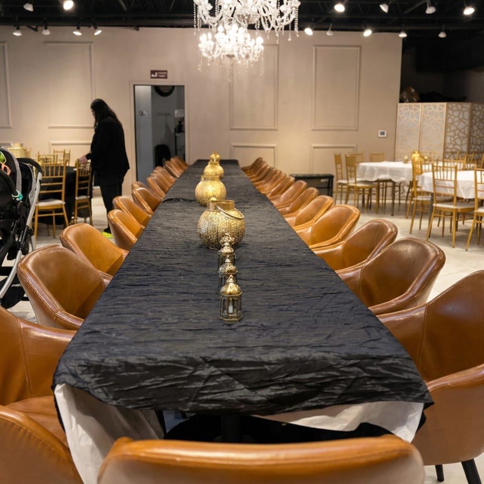 Elegant restaurant banquet hall with a chandelier, long black-draped table, brown leather chairs, and surrounding round tables.