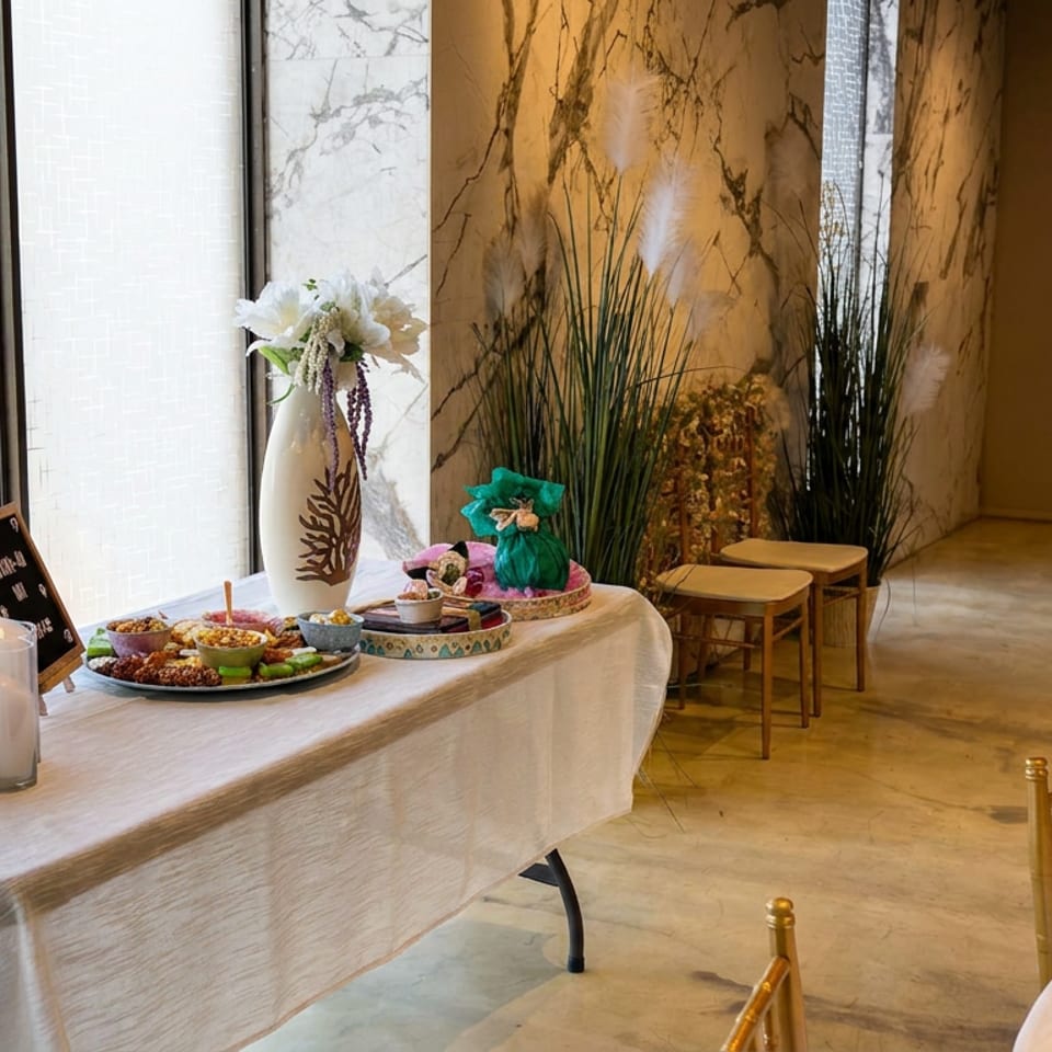 Elegant restaurant dining room with gold chairs, white tablecloths, floral centerpieces, and a dessert display on a buffet table.