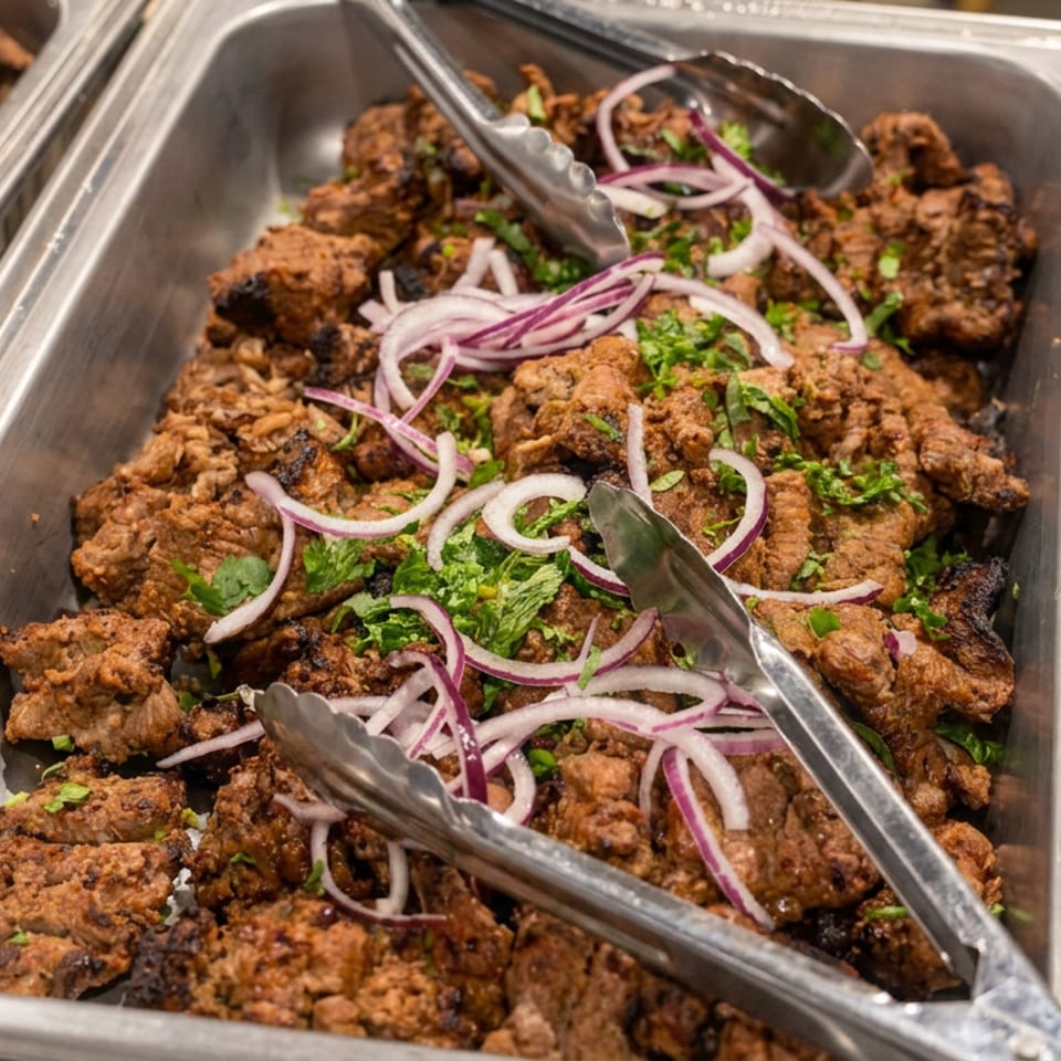 Buffet tray filled with crispy fried meat garnished with red onions, cilantro, and serving tongs.