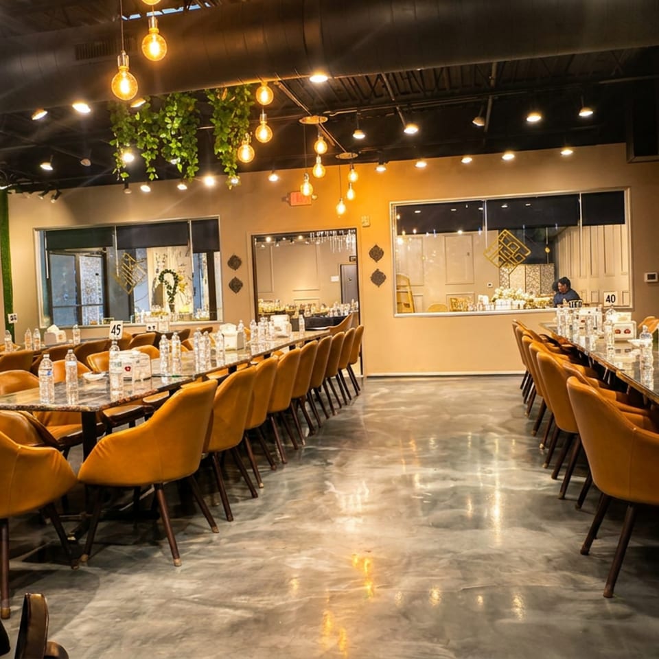 Spacious restaurant dining room with amber chairs, set tables, hanging Edison bulbs, mirrors, and polished concrete floors.